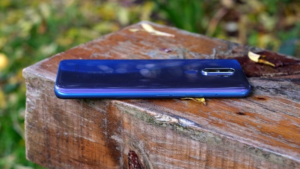 Right side edge view of a blue Oppo A9 laid facing down on a wooden surfaceTop half back panel view of a blue Oppo A9 laid facing down on a wooden surface