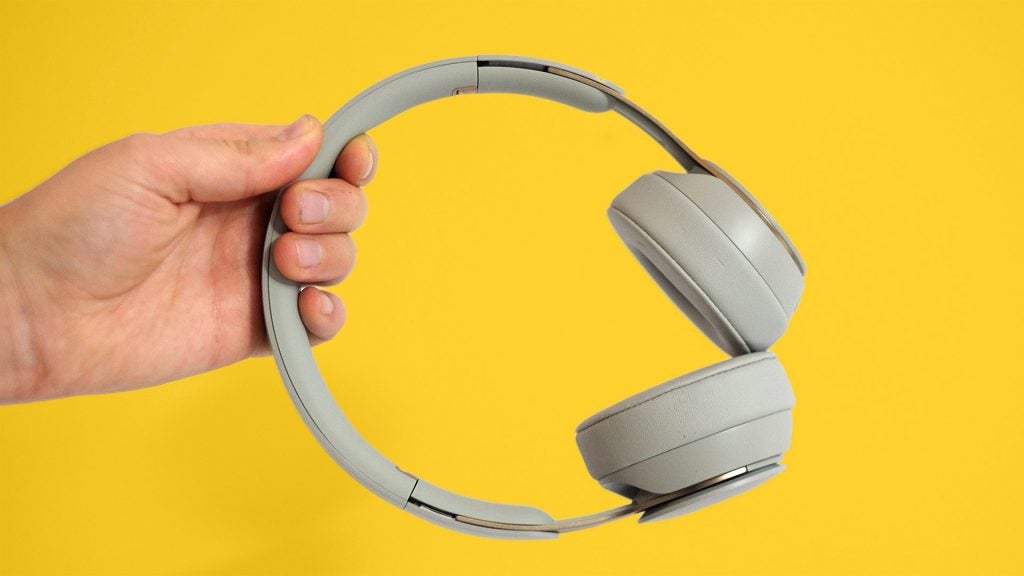Beats Solo ProWhite Beats headphones held in hand on a yellow background