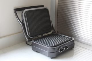 Side view of a gray-black Cuisinart GR47BU Griddle-Grill kept on a kitchen platform with lid open