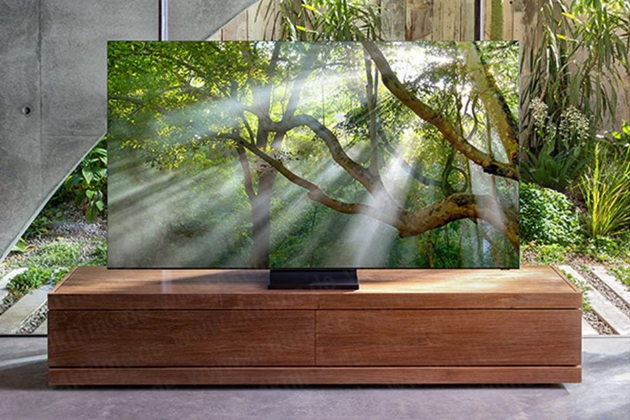 A black Samsung Q950TS TV standing on a table displaying a picture of a forest