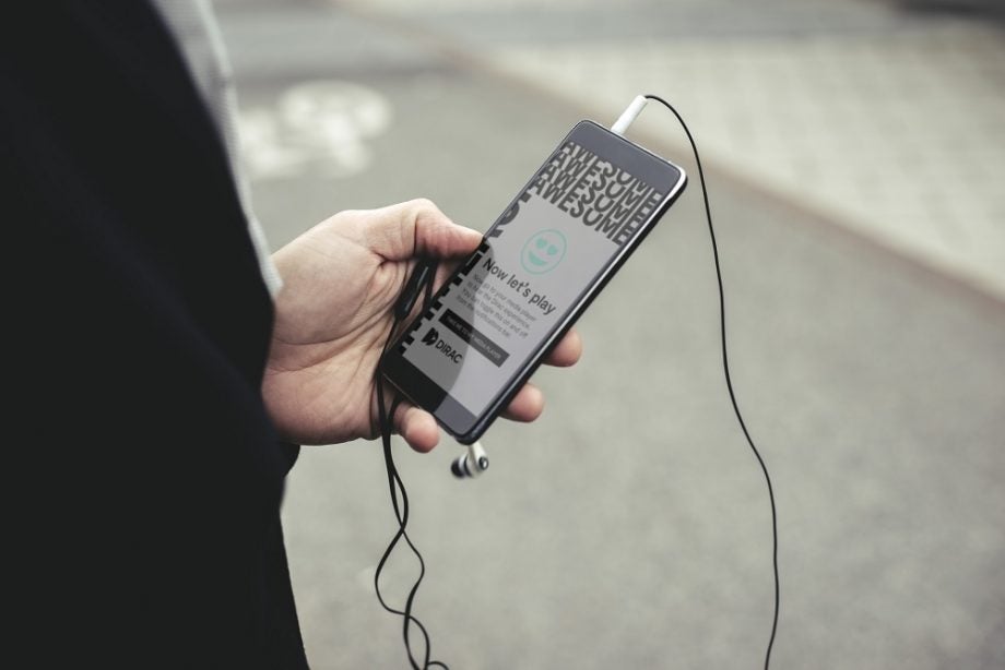 A black smartphone held in hand with earphones connected displaying Dirac app's homescreen