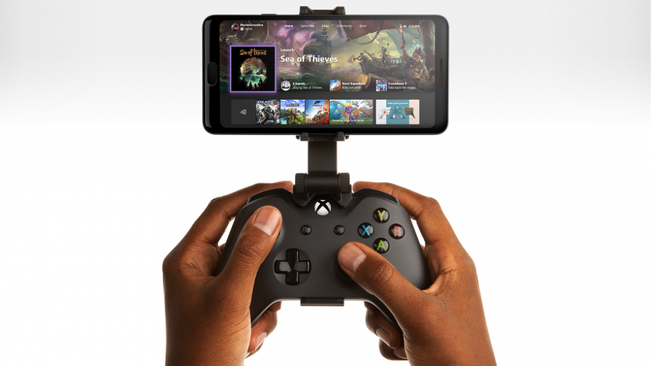 A black Xbox controller held in hand with a smartphone attached to it on a white background displaying games