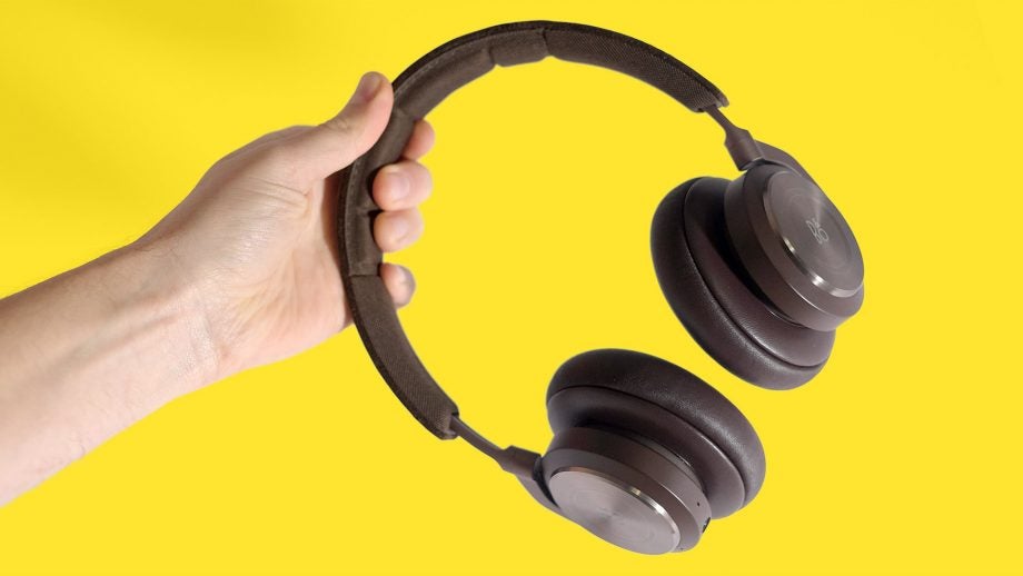 Black B&O headphones held in hand on a yellow background