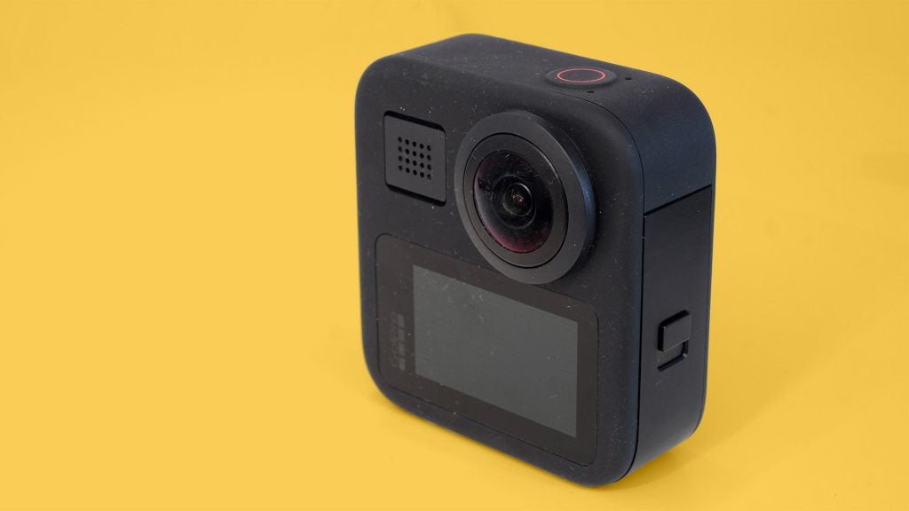 Right angled view of a gray GoPro Max camera standin on a yellow background