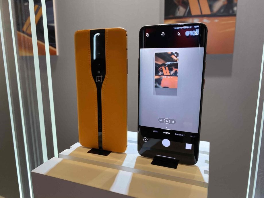 Two One Plus smartphones standing on a table showing front and back panel view