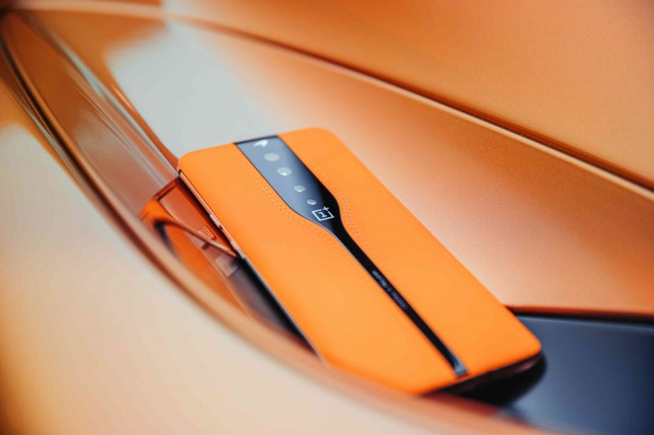 Picture of an orange-black One Plus smartphone placed facing down on an orange background