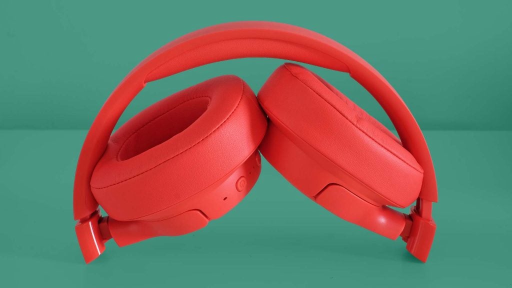 Red JBL Tune 750BTNC headphones standing on a green background with earcups folded