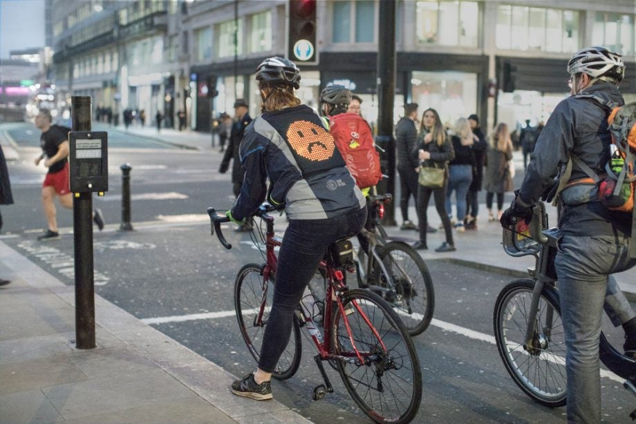 Picture of a street with a woman on cycle wearing Ford emoji jacket
