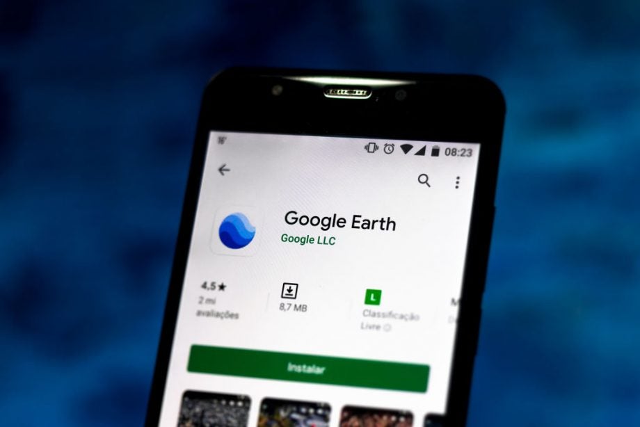 A black smartphone standing on blue background displaying Google Earth app on Play Store