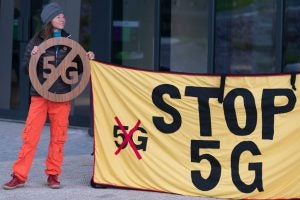 A woman holding a 5G stop sign, and a corner of a banner that says 5G