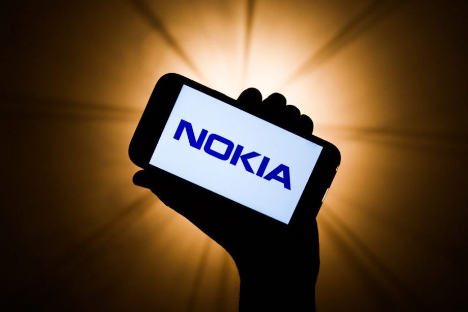 A wallpaper of a smartphone held in hand displaying Nokia logo, all black on a dawn background