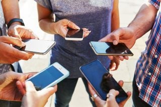 A picture of five friends standing in a circle holding smartphones