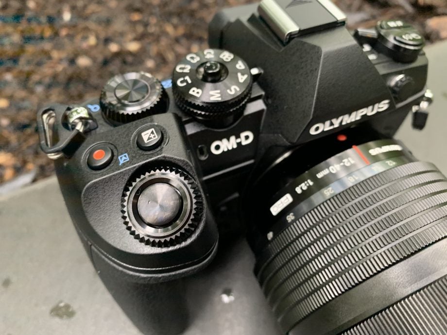 Top front view of a black Olympus OM-D E-M1 Mark III camera placed on ground