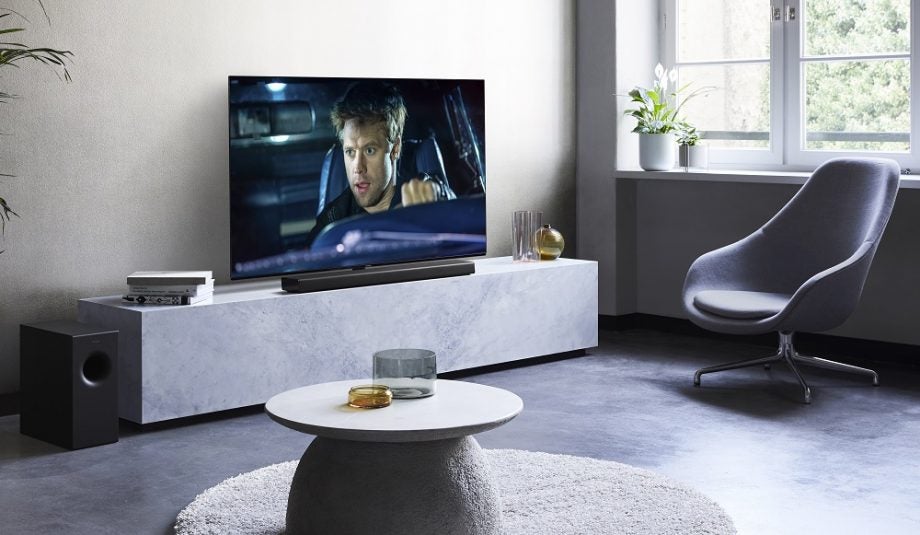 A black Panasonic HTB400 K soundbar kept on a white shelf in front of a TV in a living room