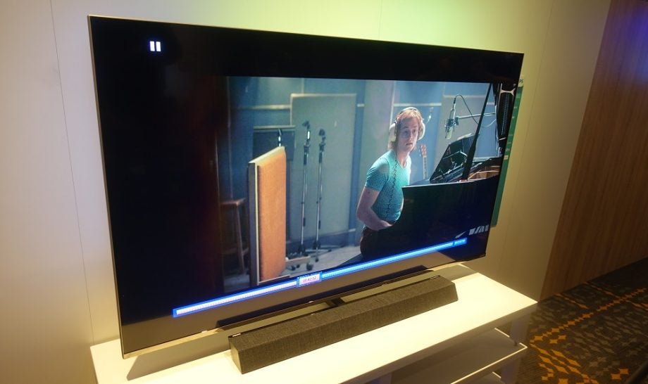 A silver Philips 55PSU9435 TV standing on a table displaying a guy playing piano