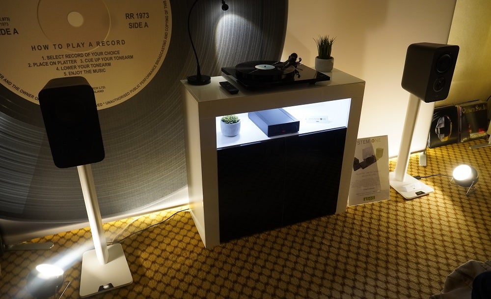 Two black Rega System One speakers standing on either sides of a table