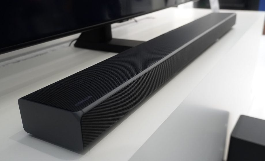 Picture of a black Samsung Q soundbar kept on a white table in front of a TV