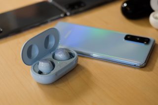 Blue Samsung Galaxy Buds Plus resting in it's case beside a Samsung Galaxy S20 on a table