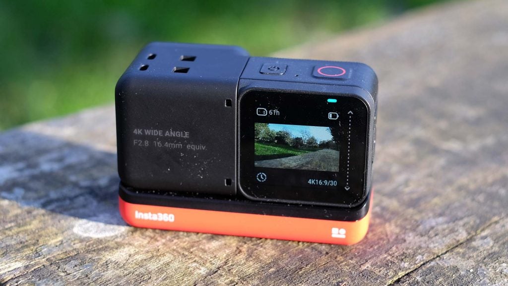 A black-red Insta 360 One R camera standing on wooden surface