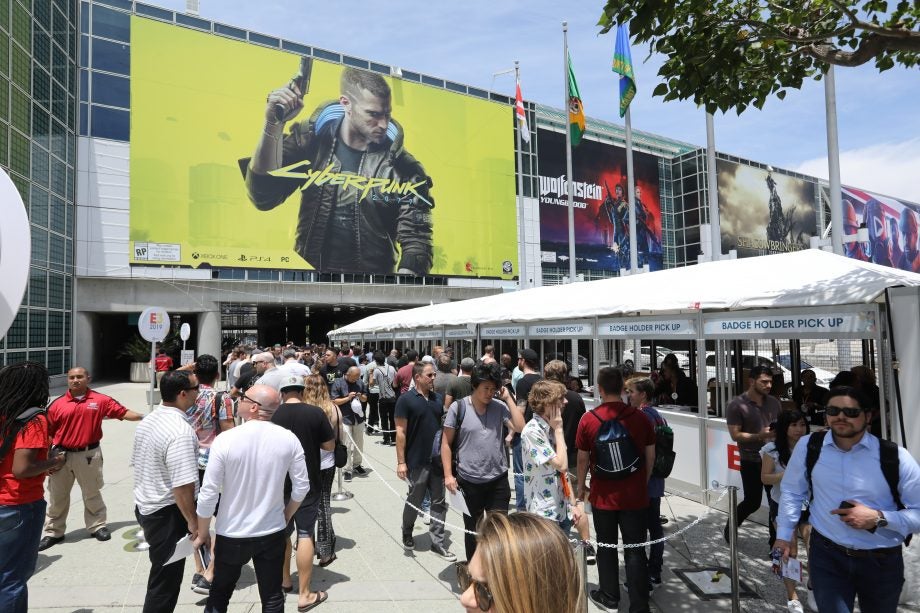 A picture of a street full of people with a banner of Cyberpunk 2077 pasted on a building