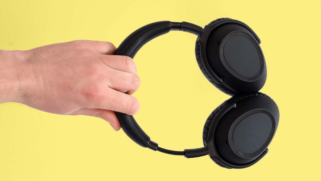 A picture of black headphones held in hand on a yellow background