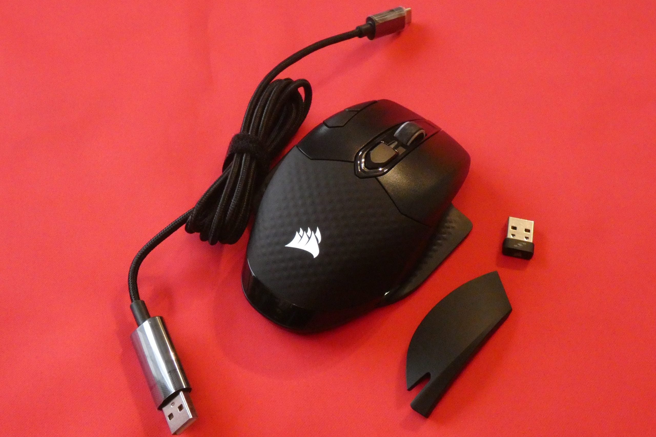 Corsair Dark Core RGB Pro SEA black Core Pro SE mouse kept on a red background with it's adapter and cables
