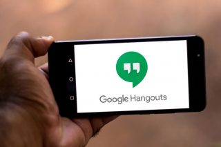 A black smartphone held in hand horizontally displaying Google Hangouts wallpaper