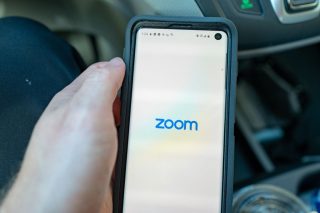 A black smartphone held in hand displaying Zoom written on a white background