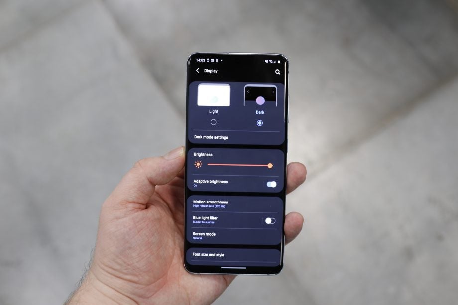 A smartphone held in hand displaying display settings menu screen