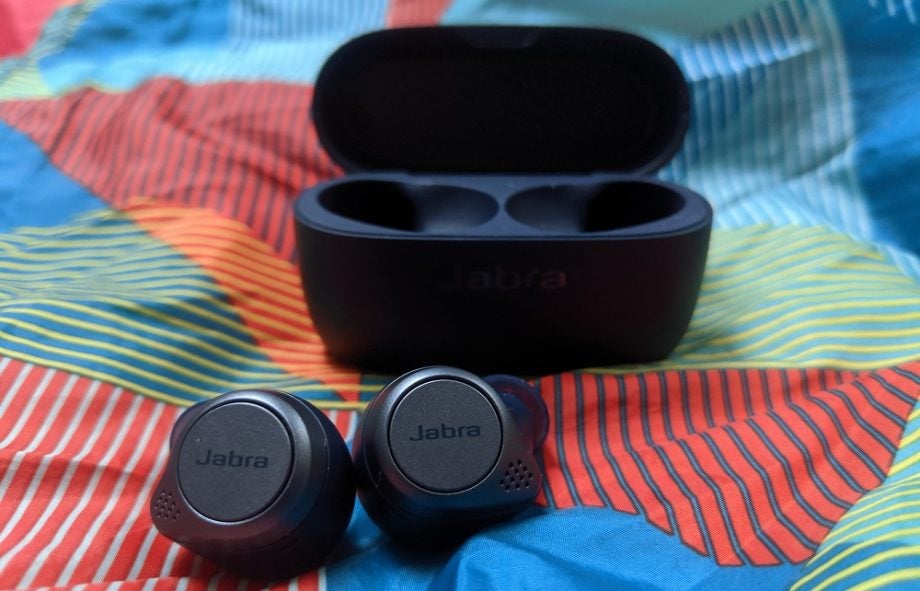 Black Jabra Elite Active 75T earbuds kept in front of it's case on a bed