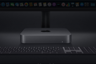 An Apple Mac Mini kept on a table behind a keyboard and beside a monitor