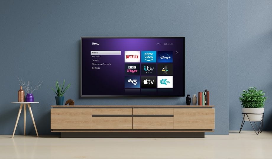A gray TV mounted to a wall displaying Roku homescreen