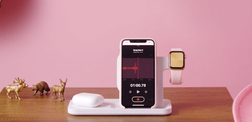 A white Logitech wireless charging dock standing on a table with a phone and a watch placed on it