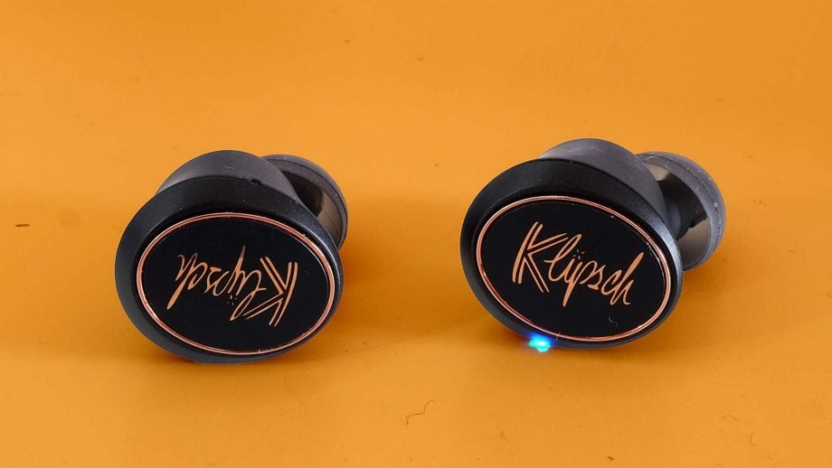 Close up image of black Klipsch earbuds kept on a table, back side view