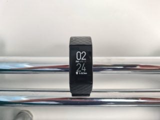 A black Fitbit tied to a bar displaying date and time