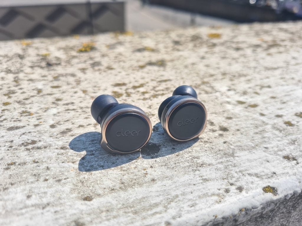 Silver-black Cleer Audio Ally Plus earbuds kept on a concrete floor