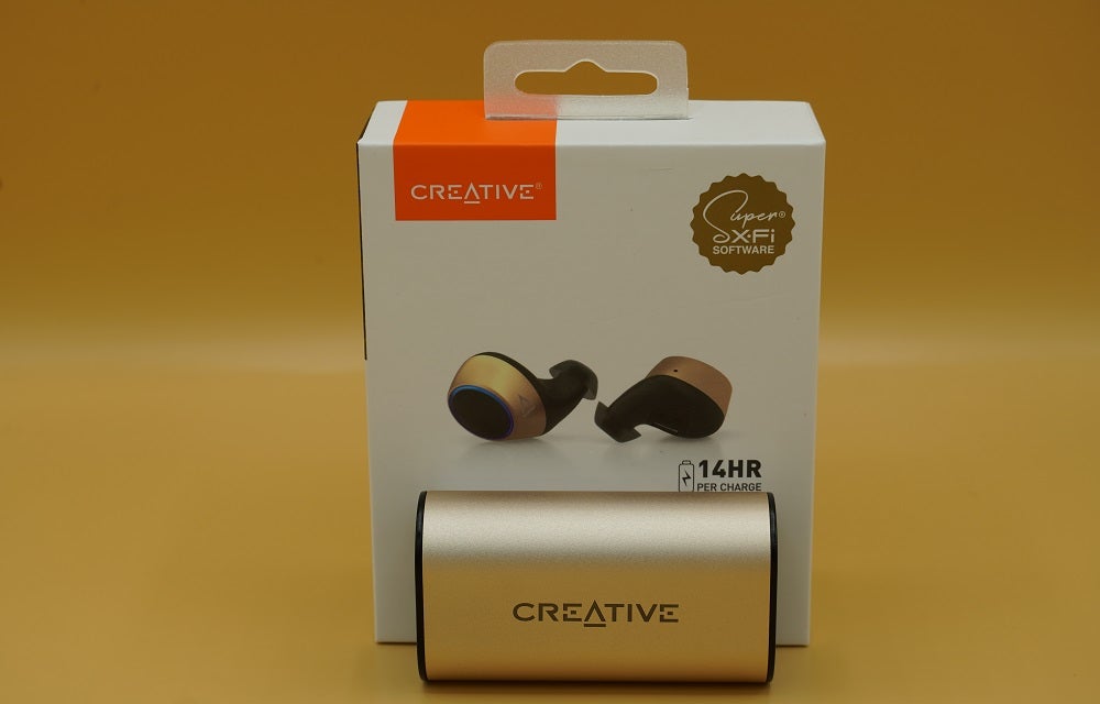 Creative Outlier Gold earbud's case standing against it's packaging box on a tableCreative Outlier Gold earbud's case standing against it's packaging box on a table