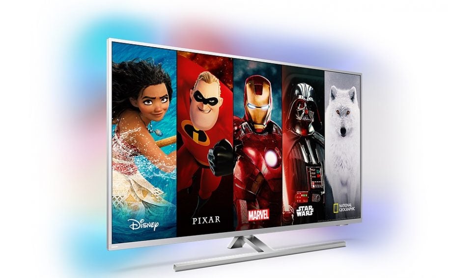 A silver Philips smart TV standing on white background displaying splitted wallpapers of Disnay, Pixar, Marvel, Star Wars and Net Geo