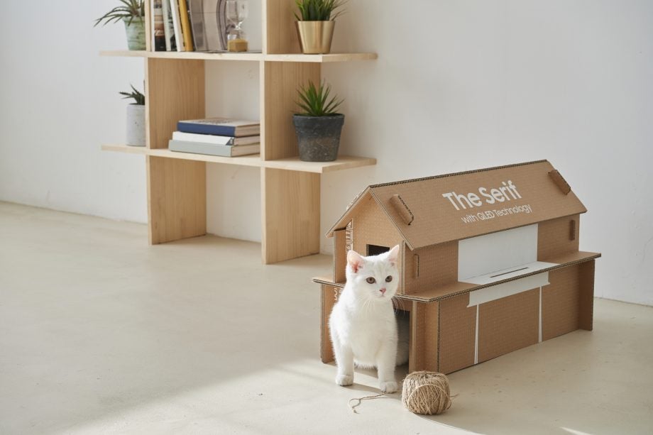 A house of a cat made of cardboard placed beside a wooden shelf