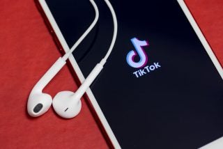 A picture of smartphone displaying TikTok screen with headphones kept on top of it