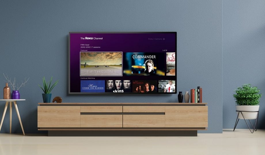 A gray TV mounted to a wall displaying Roku channel homescreen