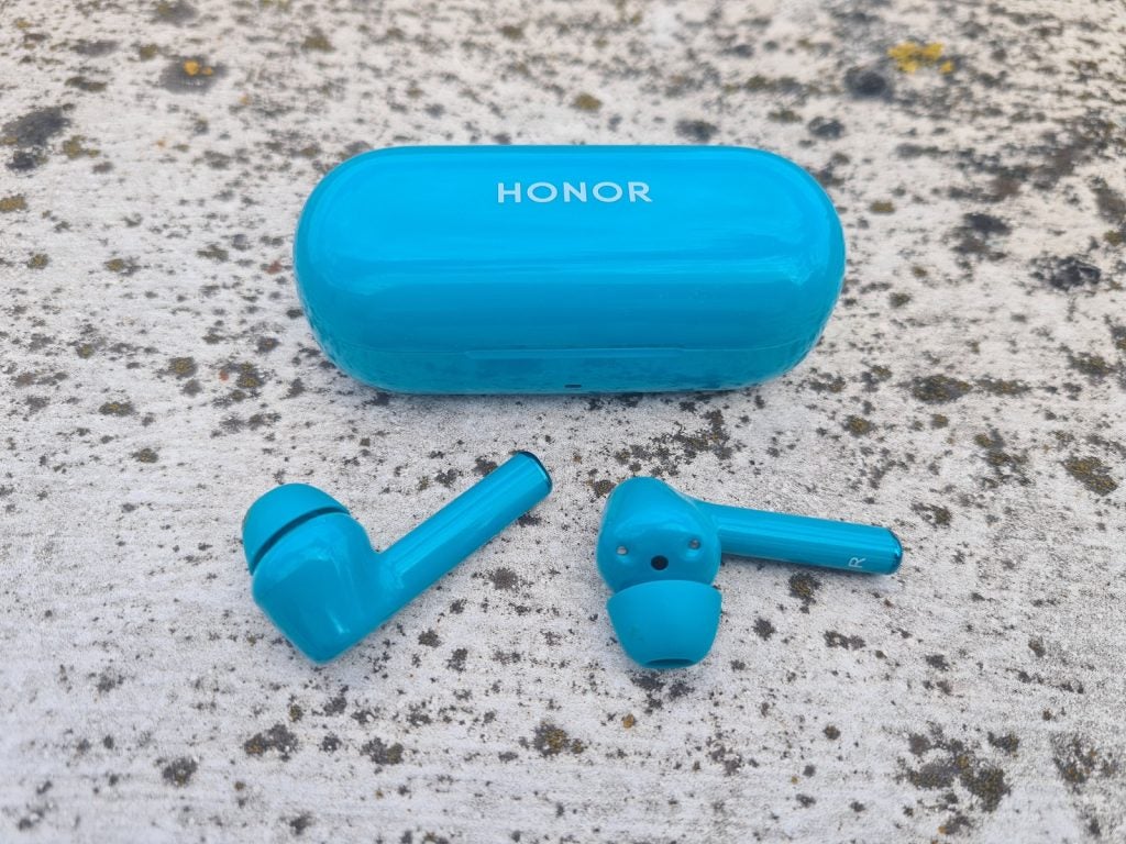 Blue Honor Magic earbuds resting with it's case behind on a concrete floor