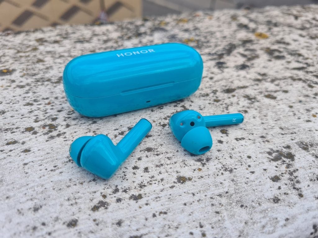 Blue Honor Magic earbuds resting with it's case behind on a concrete floor