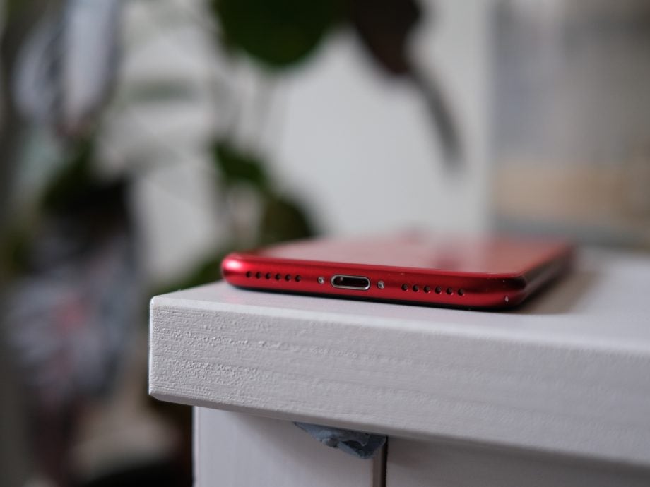 Bottom edge view of a red iPhone SE placed upside down on a white shelf
