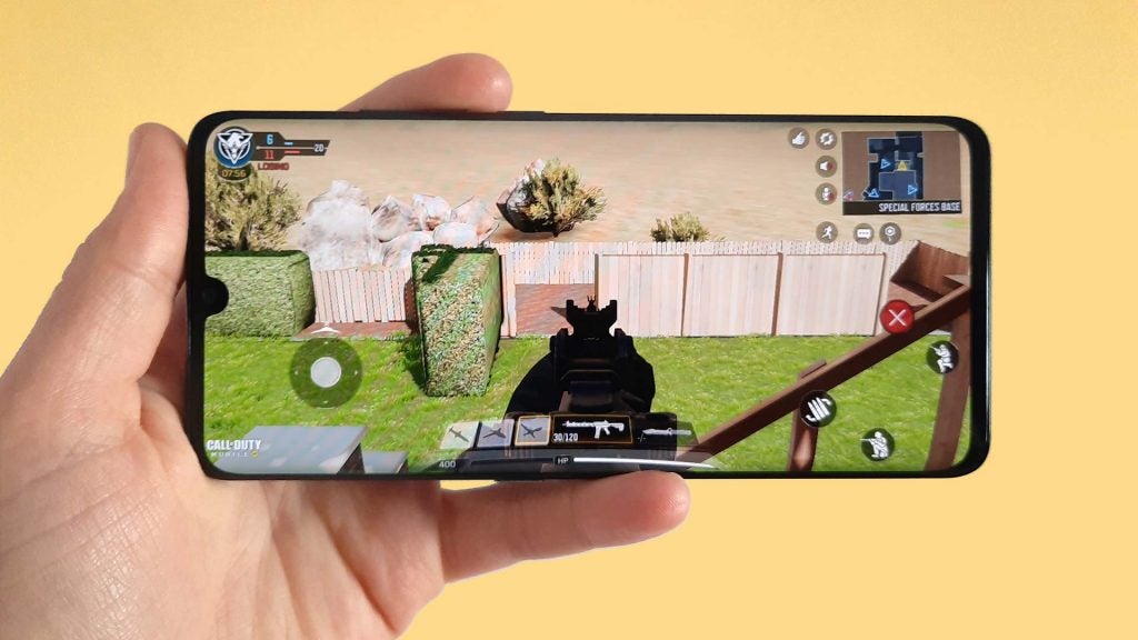 A smartphone held in hand displaying a scene from a shooting game
