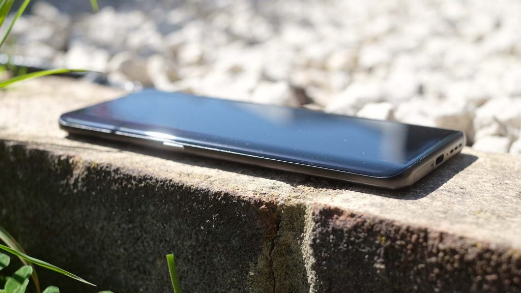 A black TCL smartphone laid on ground, side view