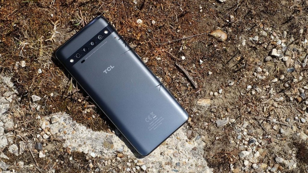 A black TCL smartphone laid upside down on ground, back panel view