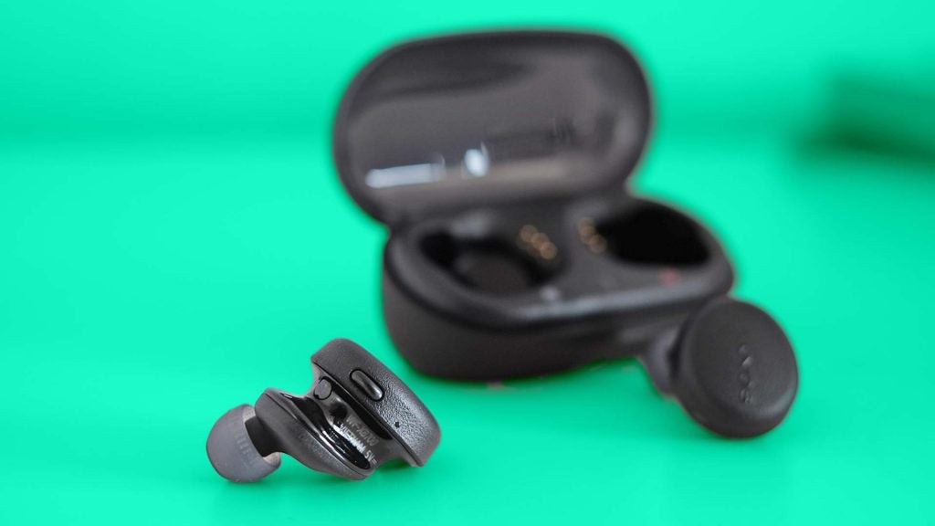 Sony WF-XB700Black WF-XB700 earbuds resting with it's case standing behind on a green background