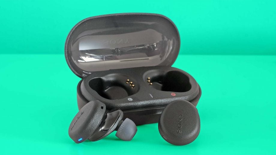 Black WF-XB700 earbuds resting with it's case standing behind on a green background