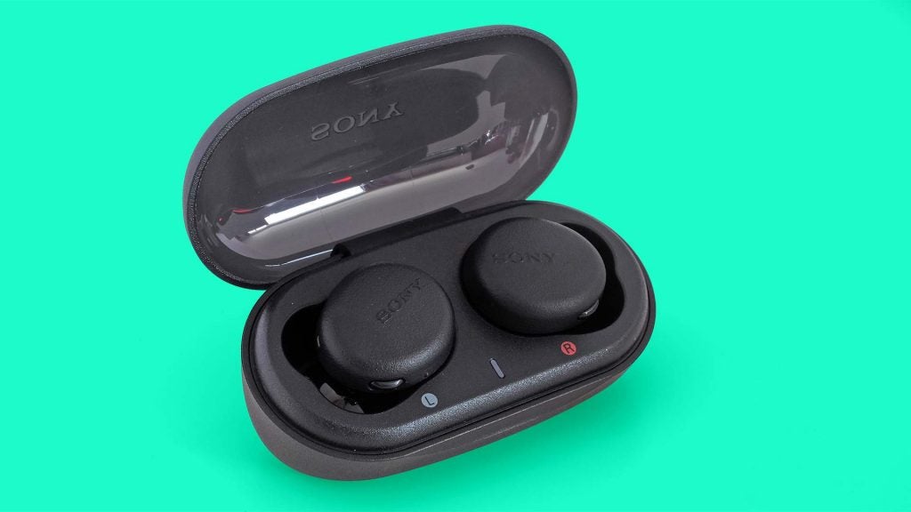 Black WF-XB700 earbuds resting in it's case on a green background